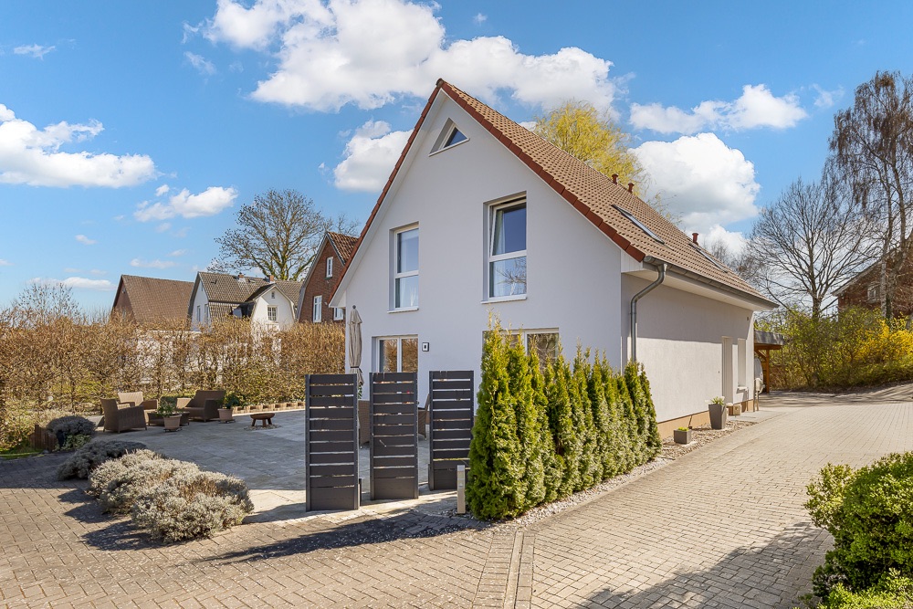 Modernes Einfamilienhaus mit Garten, Terrasse und Sichtschutz an einem sonnigen Tag.