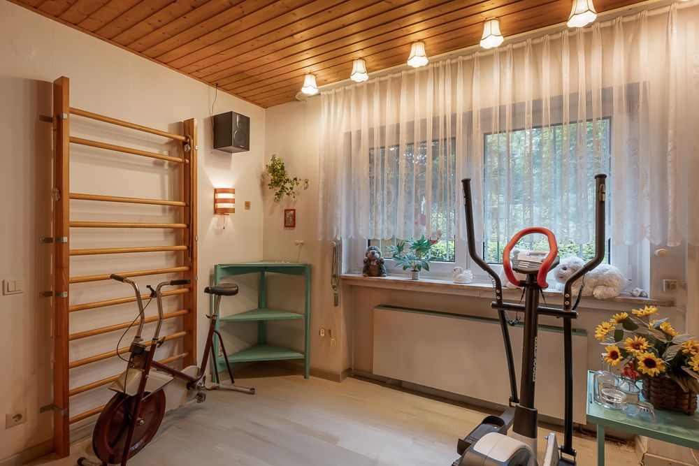 Helles Zimmer mit Sprossenwand, Hometrainer, Fenster mit Gardinen und Dekoration auf der Fensterbank.