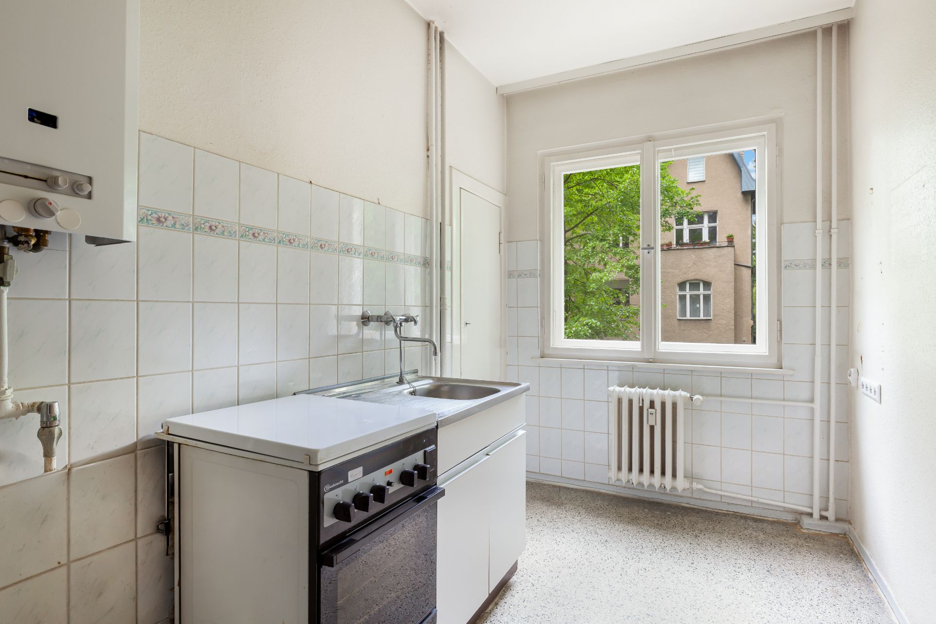 Helle, kleine Küche mit Herd, Spüle und großem Fenster mit Blick nach draußen.