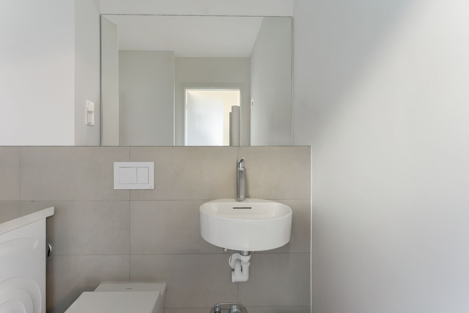 Modernes Badezimmer mit rundem Waschbecken, Wandspiegel und neutralen Fliesen.