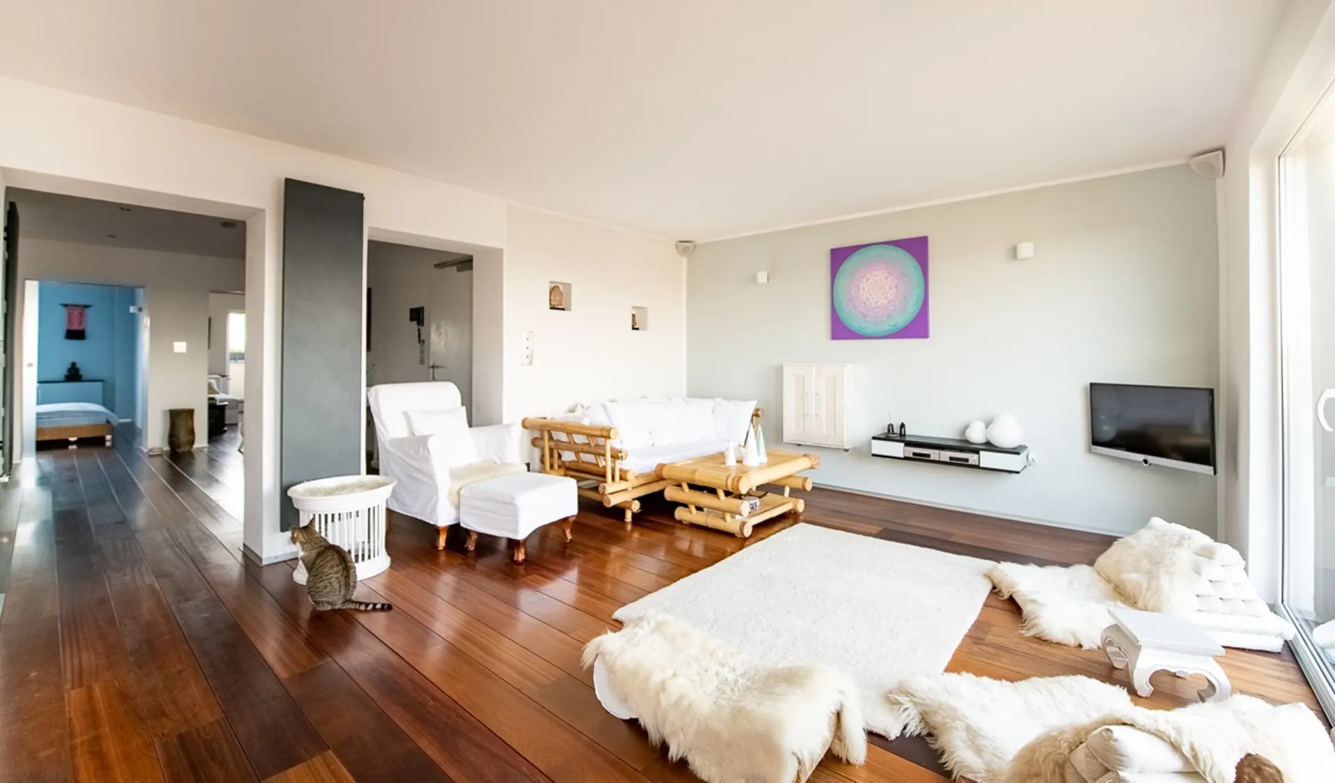 Helles Wohnzimmer mit Holzfußboden, weißen Möbeln und einer Katze auf dem Boden.