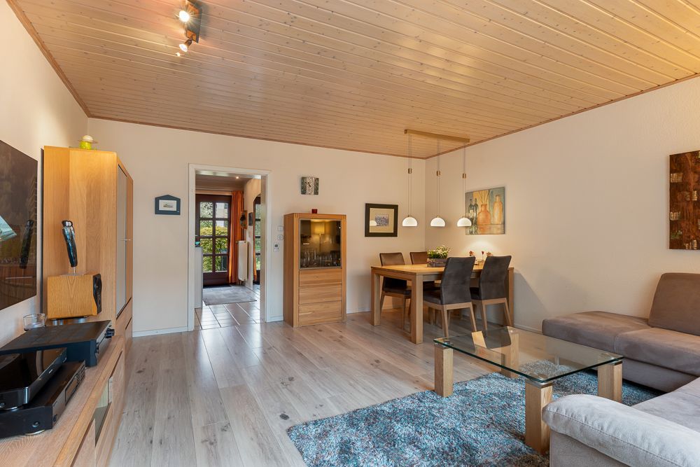 Helles Wohnzimmer mit Holzboden, Sofa, Esstisch, Vitrine und Glastisch.