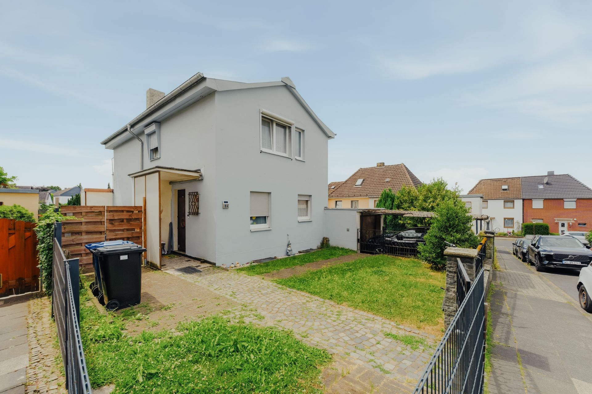 Zweistöckiges Wohnhaus mit Einfahrt, Grünfläche und Mülltonne vor dem Haus.