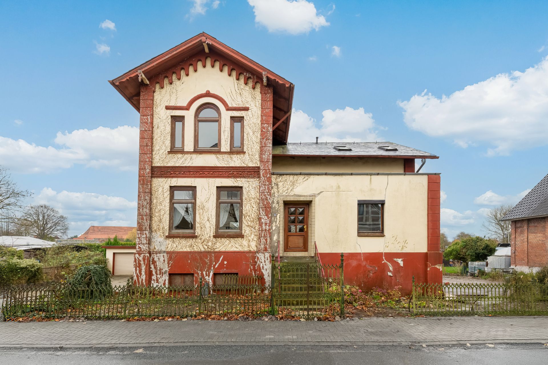 Zweistöckiges Wohnhaus mit bröckelnder Fassade, kleinem Garten und Zaun an der Straße.