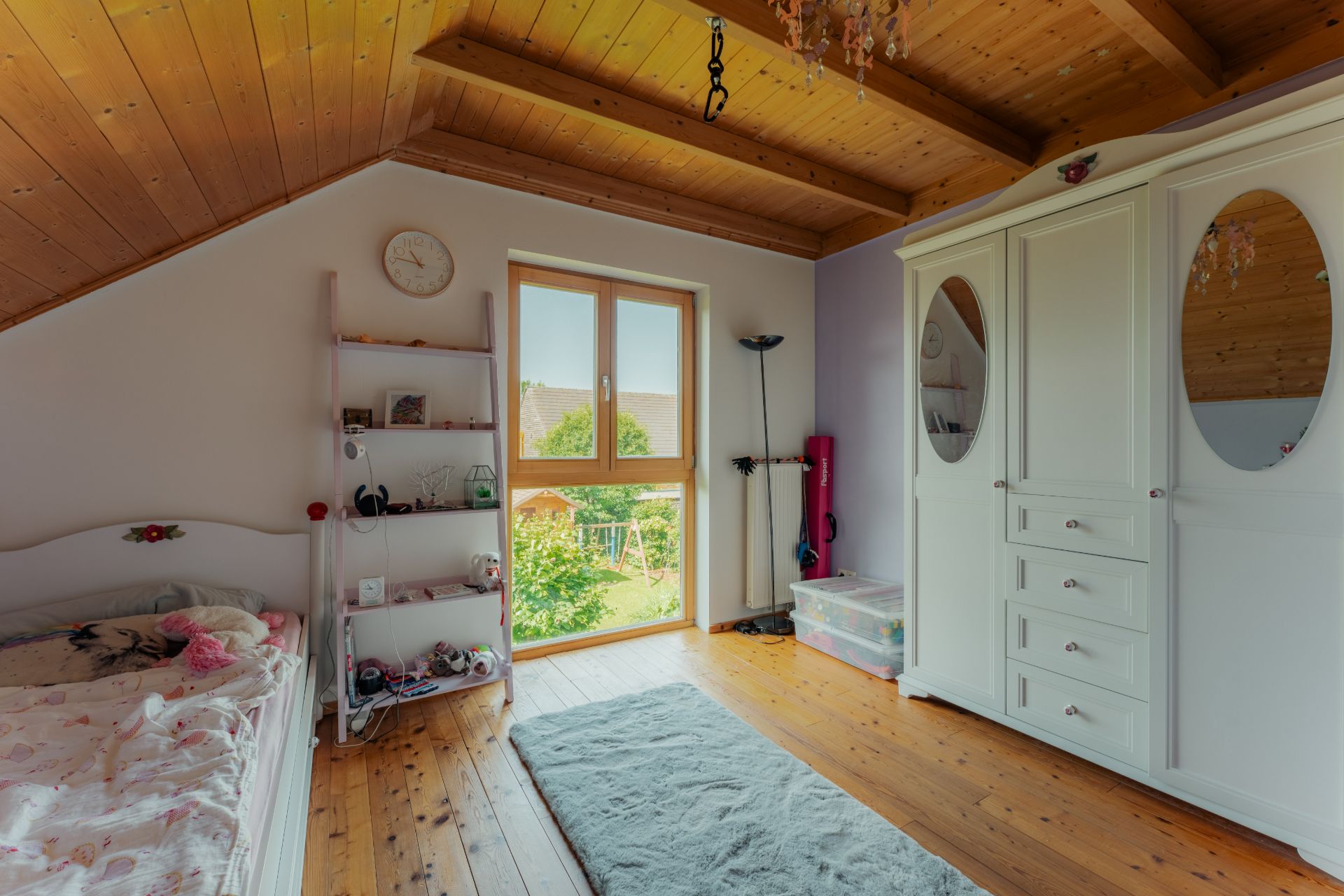 Helles Kinderzimmer mit Holzdecke, Bett, Regal, Teppich und großem weißen Schrank.
