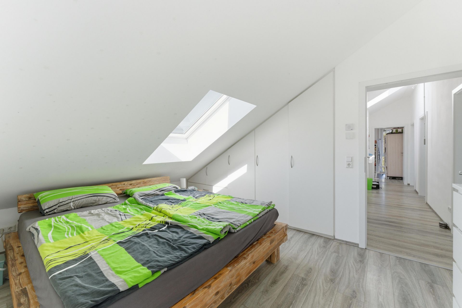 Helles Schlafzimmer mit Dachfenster, Doppelbett und Einbauschränken unter einer Dachschräge.