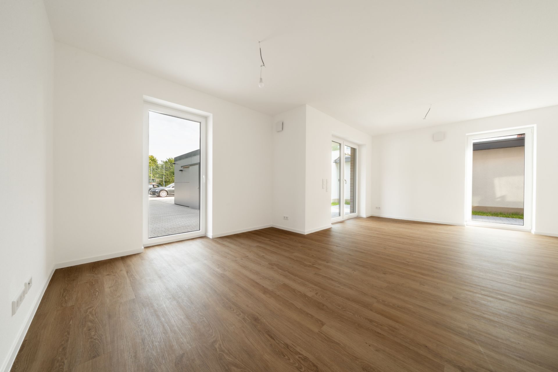 Helles, leeres Zimmer mit Holzfußboden und drei bodentiefen Fenstern.