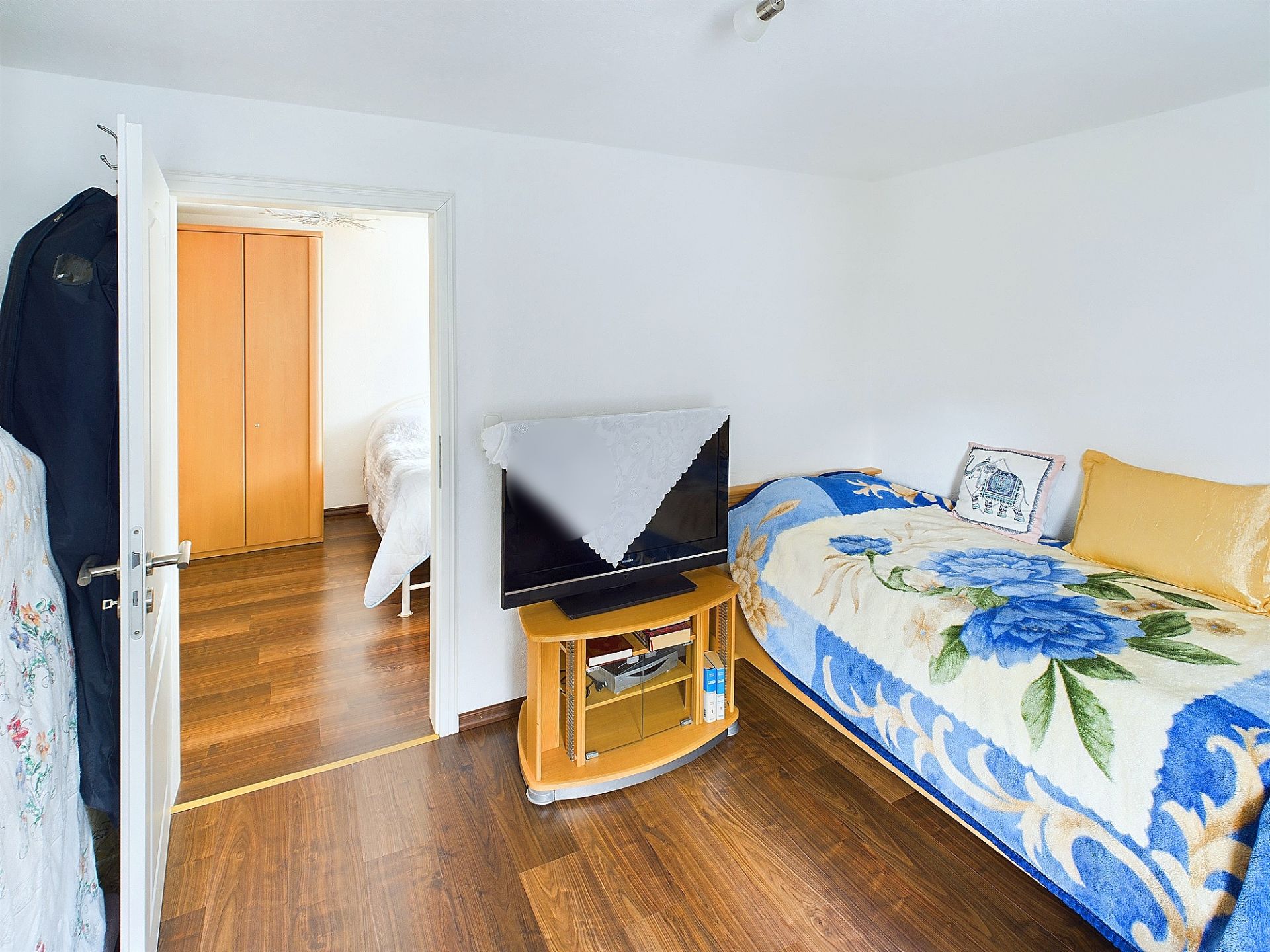 Kleines Zimmer mit Einzelbett, TV auf Holztisch und Blick durch offene Tür in ein weiteres Zimmer.