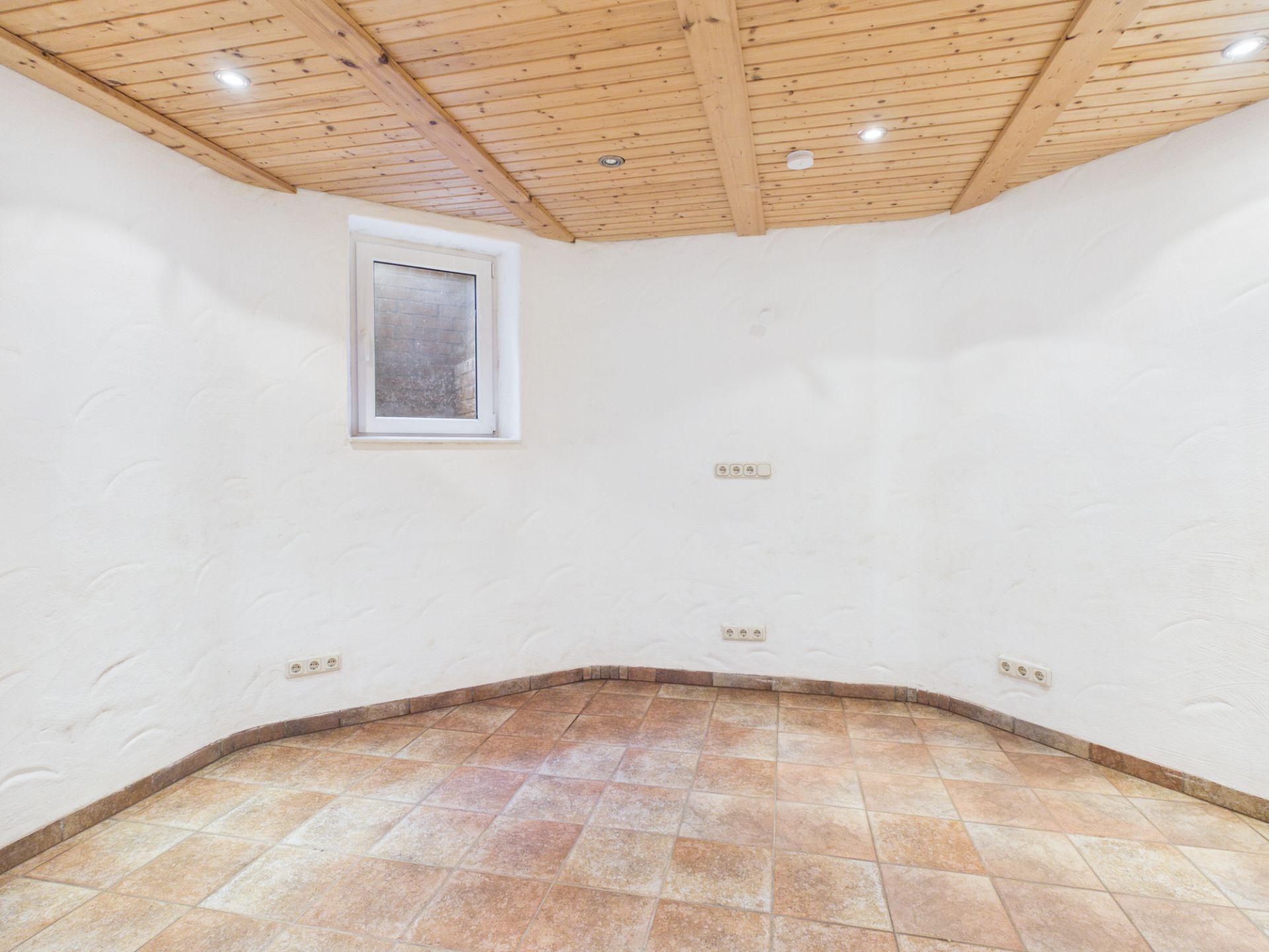 Leerer Raum mit gefliestem Boden, weißer Wand, Holzdecke und kleinem Fenster.