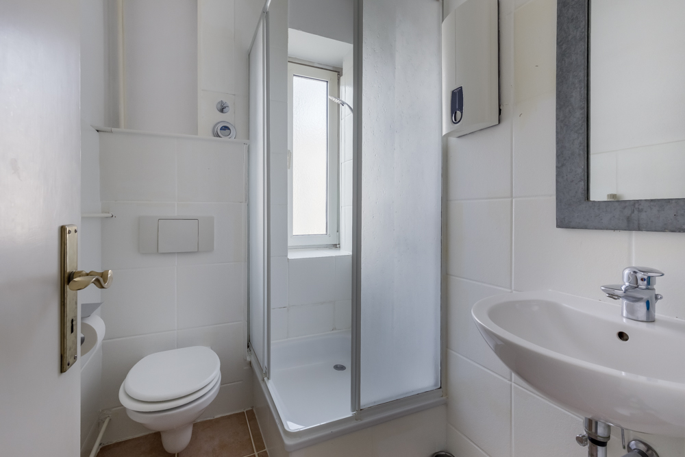 Kleines Badezimmer mit Dusche, Toilette, Waschbecken und Spiegel, helle Fliesen.