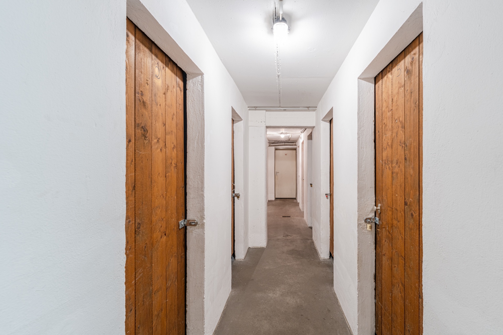 Flur mit mehreren Holztüren und weiß gestrichenen Wänden, Deckenlampe brennt.