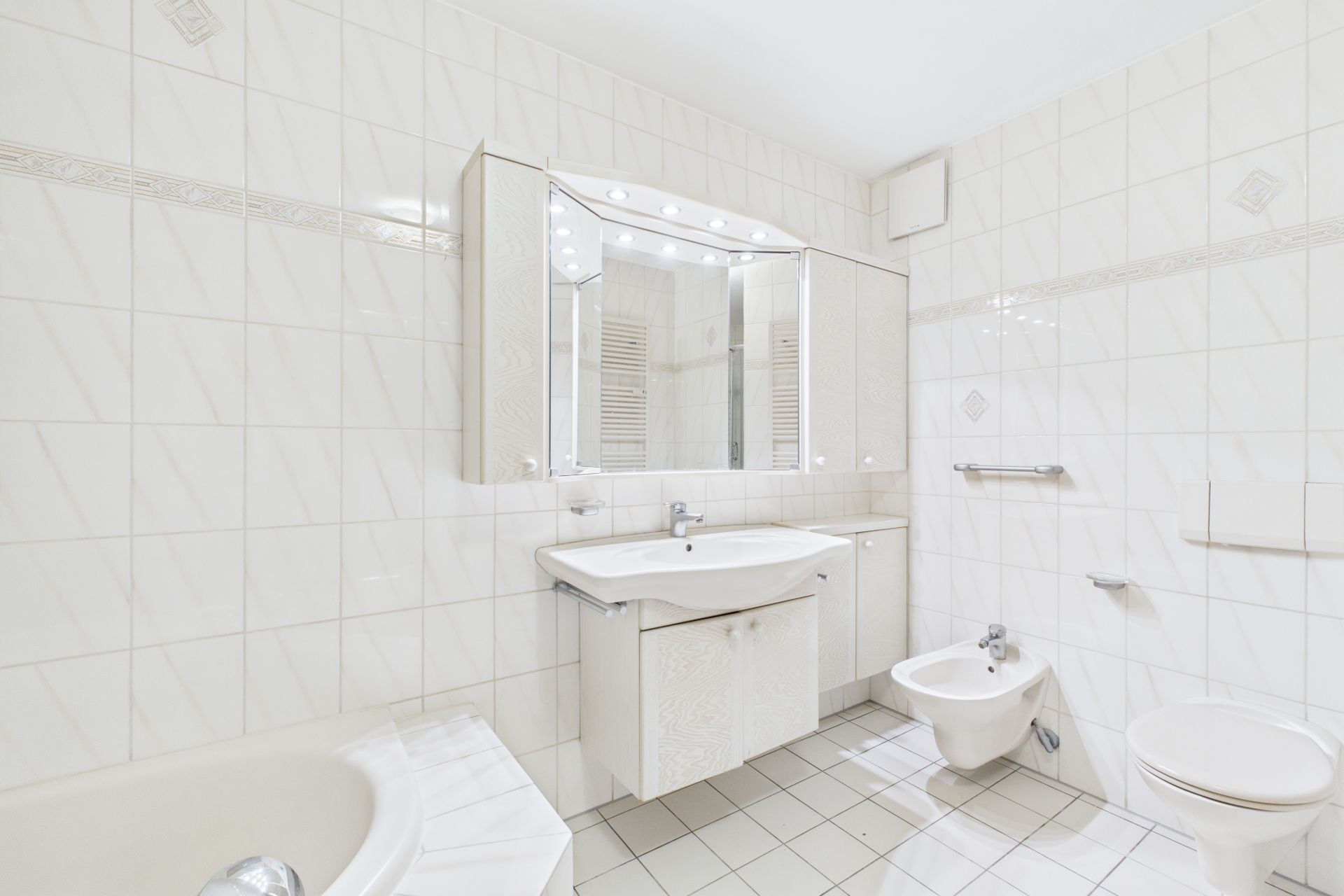 Helles Badezimmer mit Waschtisch, Spiegel, Toilette, Bidet und Badewanne.