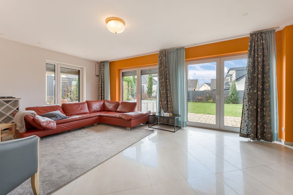Helles Wohnzimmer mit rotem Ecksofa, großen Fenstern und Blick auf den Garten.