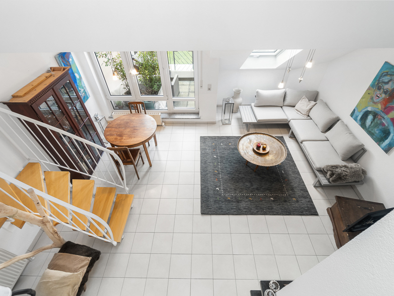 Helles Wohnzimmer mit Sofa, rundem Tisch, Teppich und Treppe, Blick von oben.