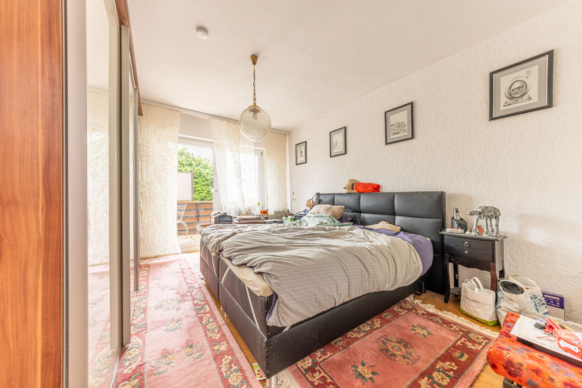 Schlafzimmer mit Doppelbett, Nachttischen, Teppich und Zugang zu einem Balkon mit Stühlen.