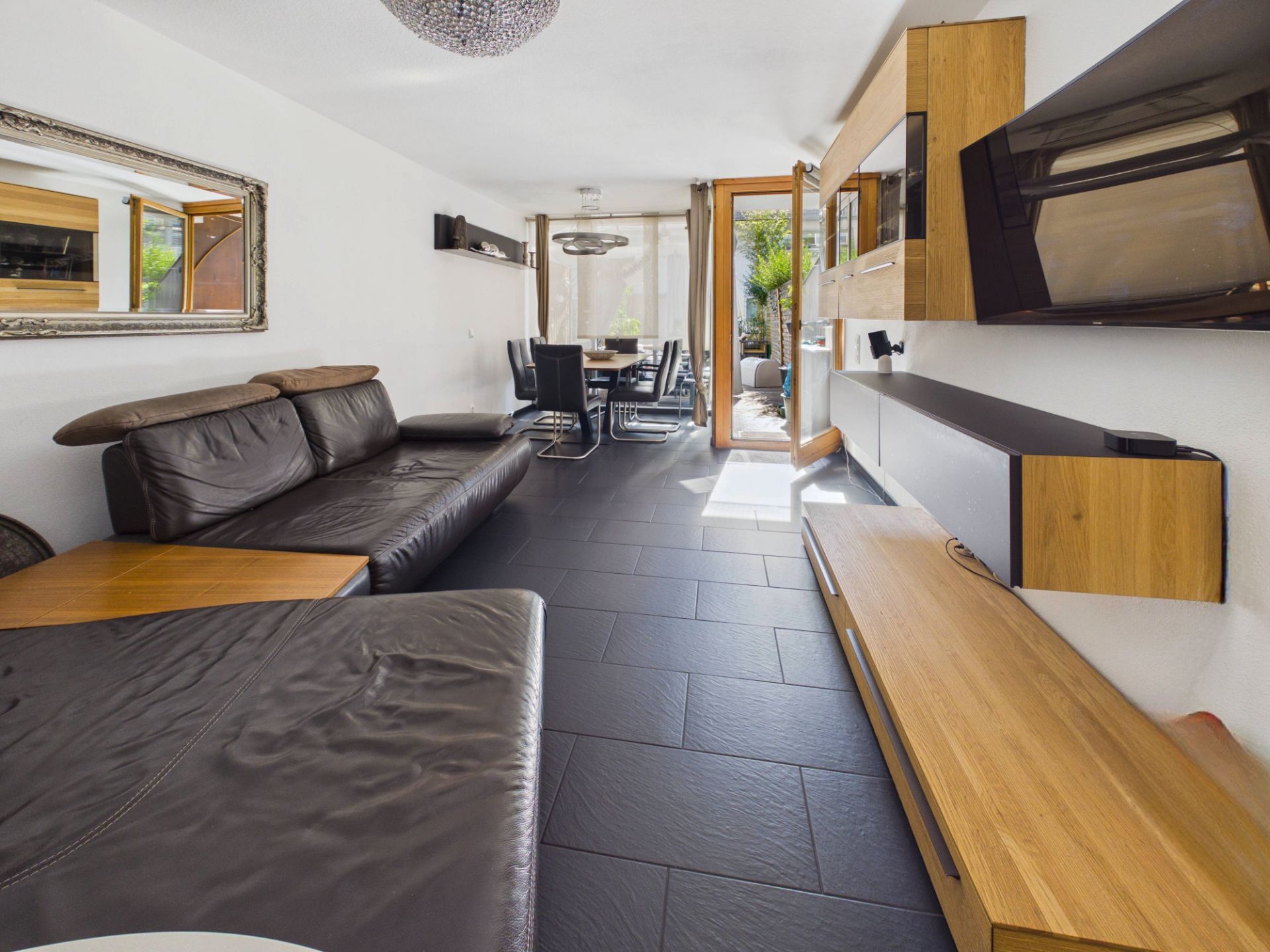 Modernes Wohnzimmer mit schwarzem Sofa, Holzmöbeln und Blick auf den Essbereich und Terrasse.