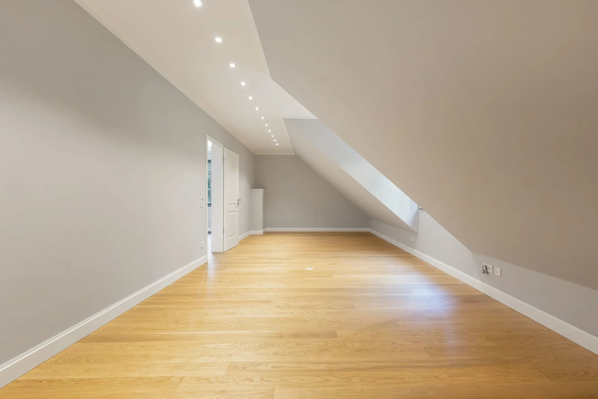 Leerer Dachgeschossraum mit Holzfußboden, grauen Wänden und Dachfenster.