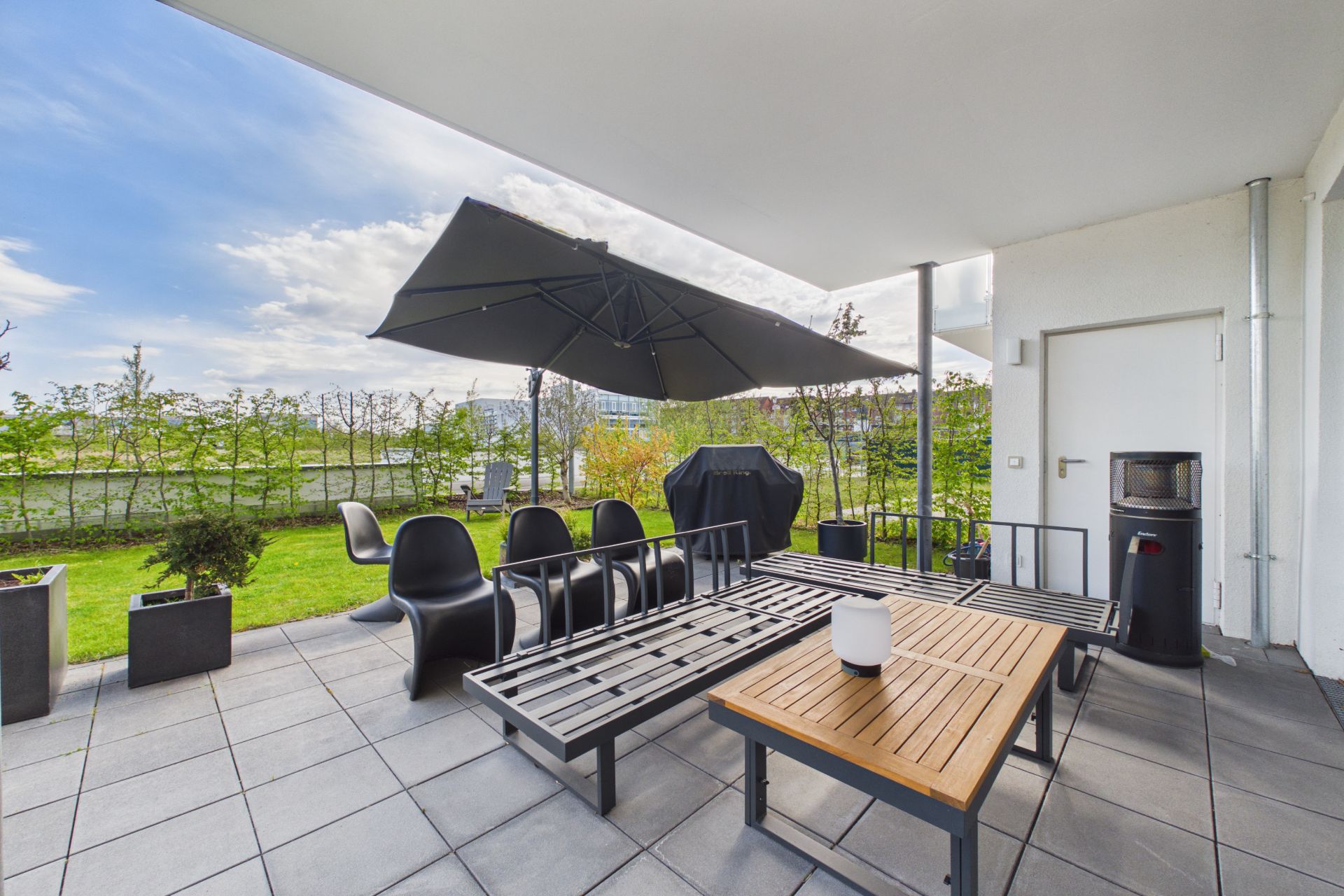 Überdachte Terrasse mit Sitzbank, Tisch, Stühlen und großem Sonnenschirm, Blick auf Garten.