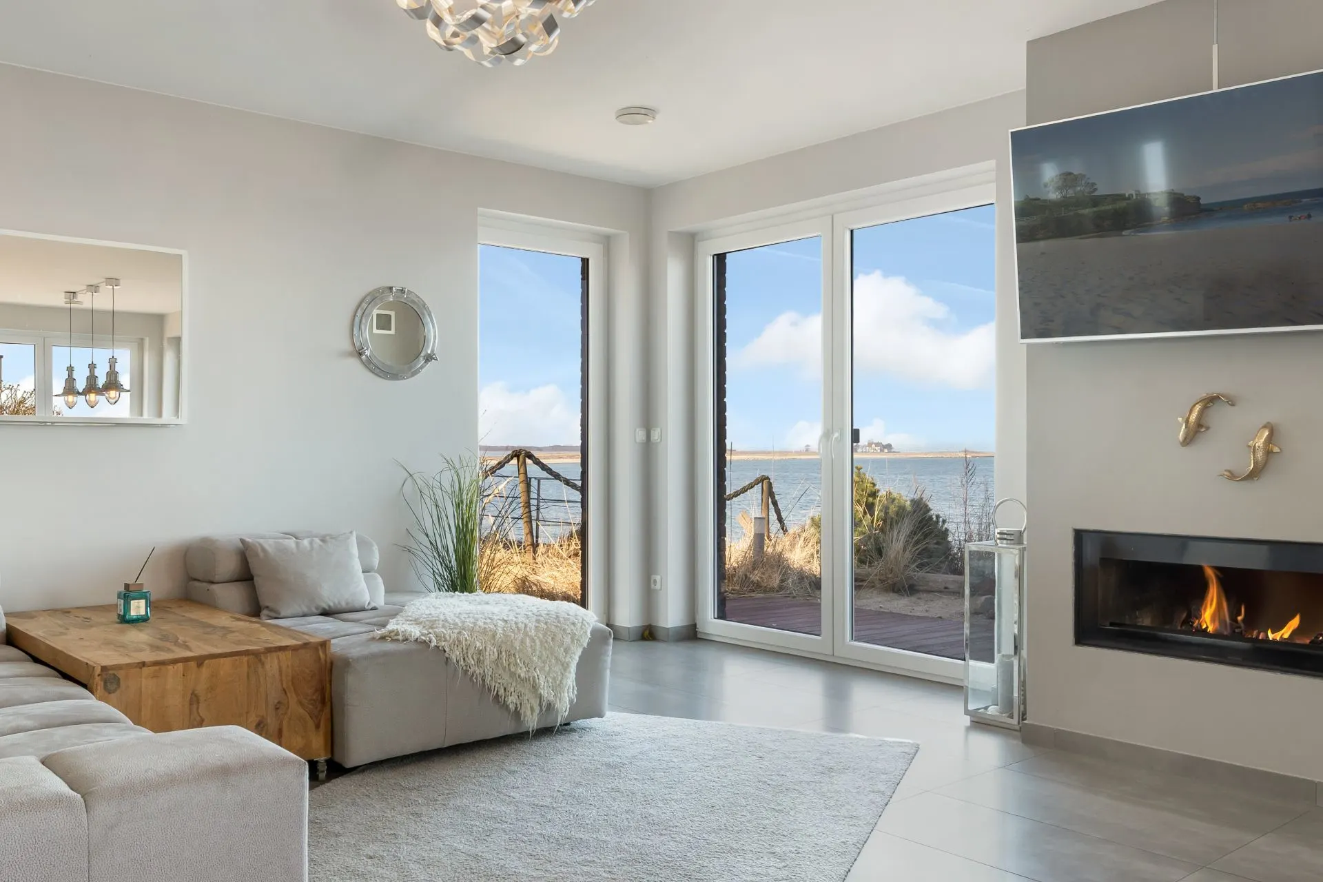 Modernes Wohnzimmer mit Sofa, Kamin und großem Fenster mit Blick auf das Wasser.
