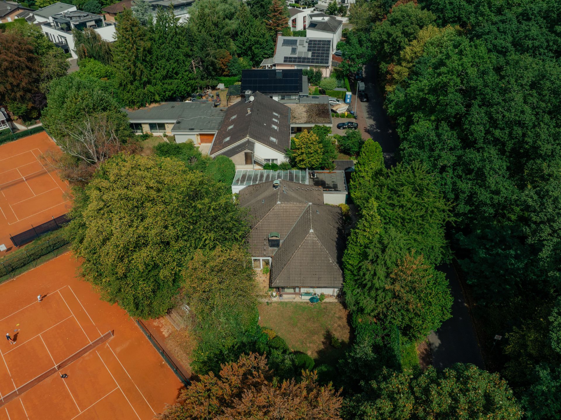 Luftbild eines Wohnhauses mit Garten, daneben Tennisplätze und viele Bäume.