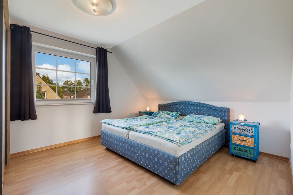 Schlafzimmer mit Doppelbett, blauem Nachttisch und großem Fenster mit Blick nach draußen.