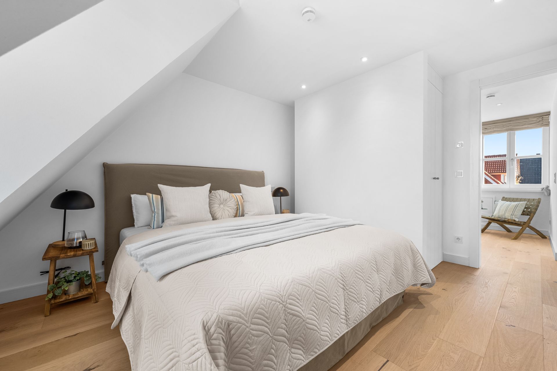 Helles Schlafzimmer mit Doppelbett, Nachttischen und Holzfußboden, Fenster im Hintergrund.