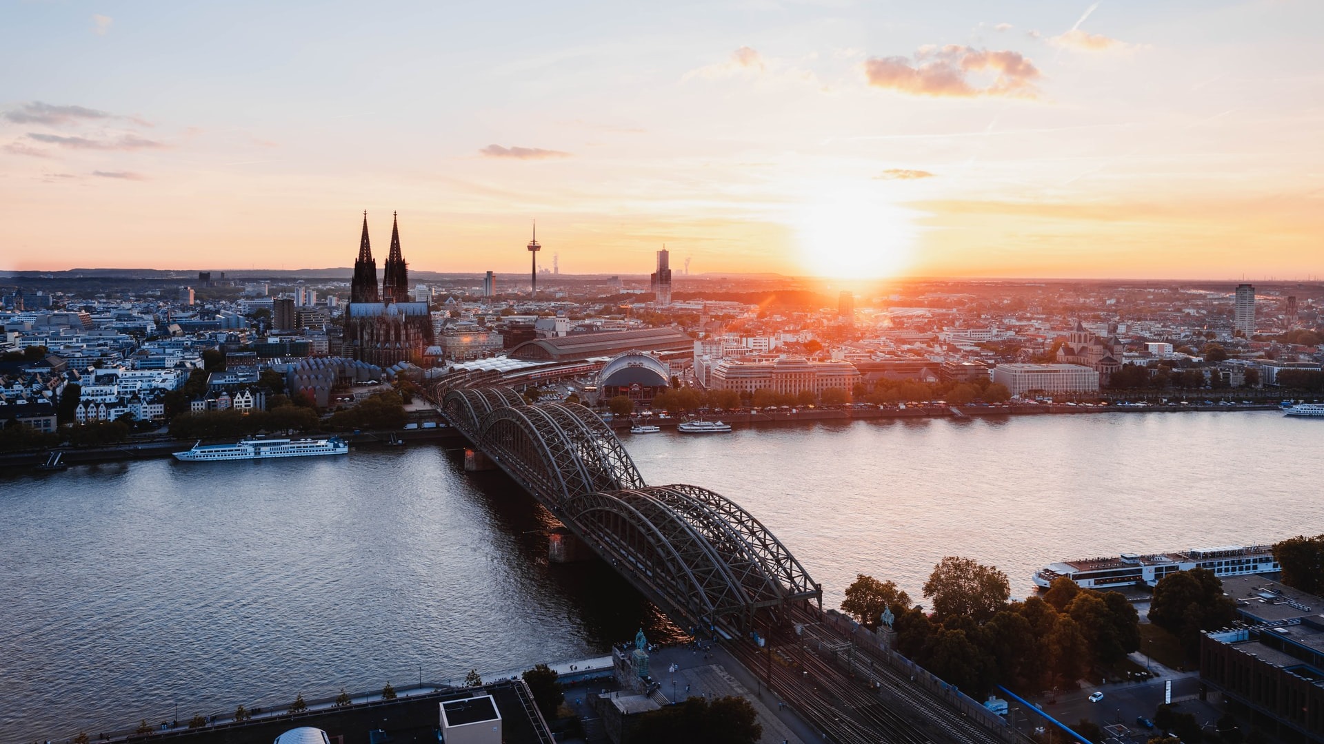 Blick auf eine Stadt mit Fluss, Brücke und Sonnenuntergang im Hintergrund.