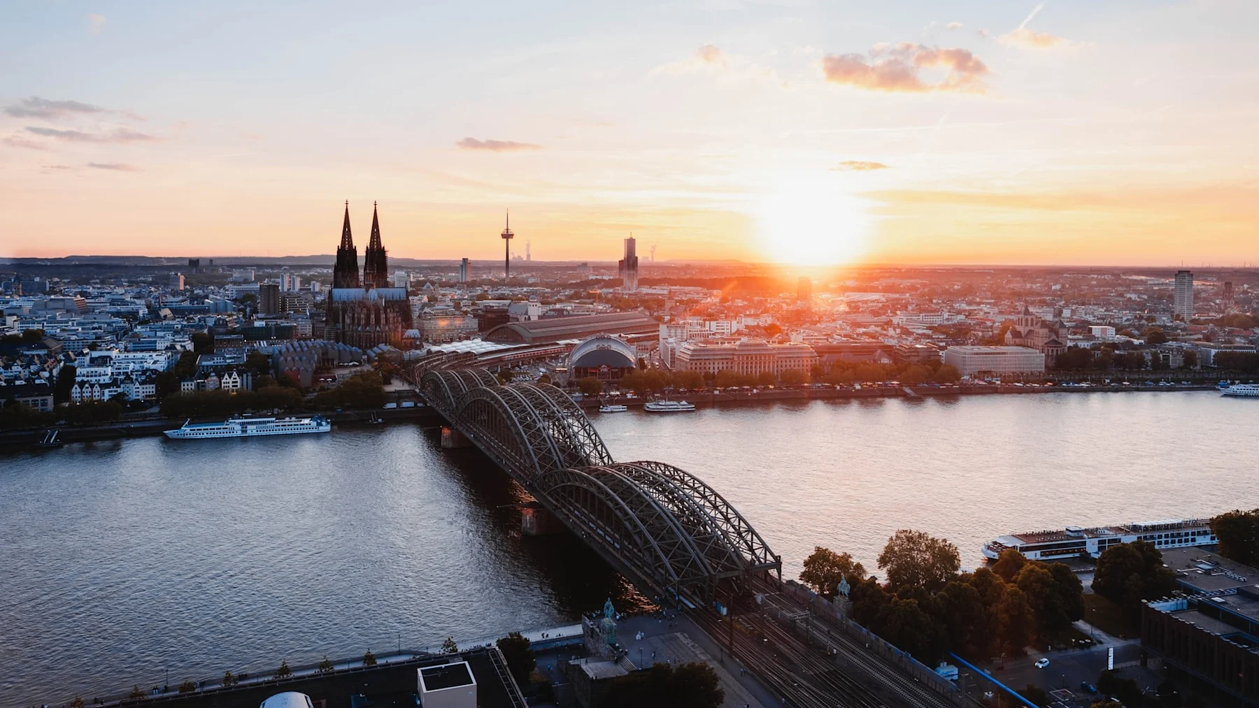 Blick auf eine Stadt mit Fluss, Brücke und Sonnenuntergang im Hintergrund.
