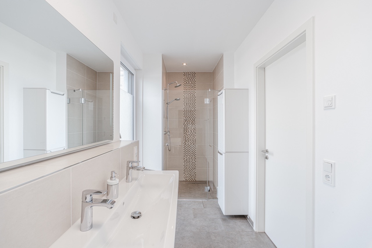 Modernes Badezimmer mit Doppelwaschbecken, großer Dusche und hellen Fliesen.