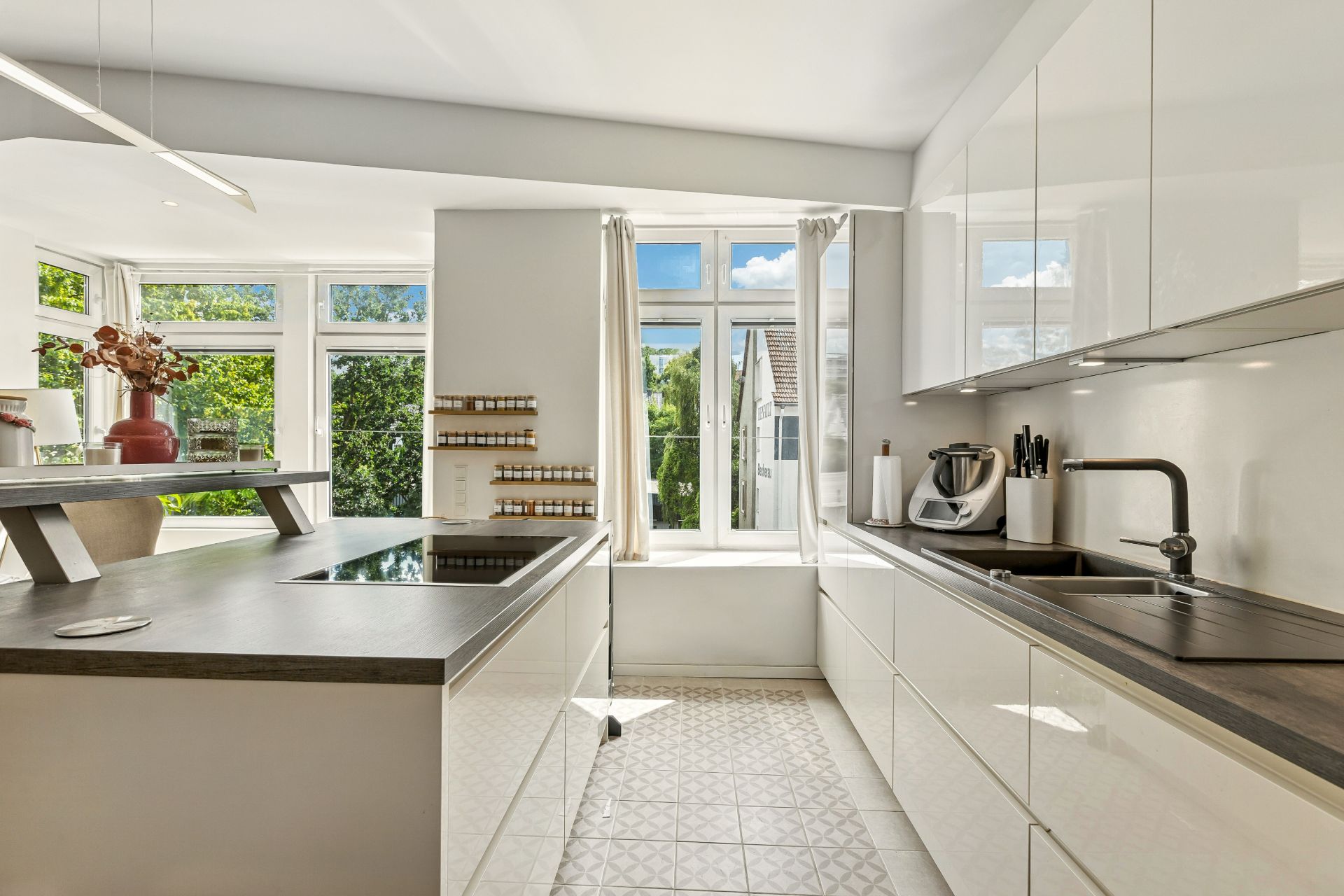 Moderne, helle Küche mit großen Fenstern, weißen Schränken und Arbeitsplatte.