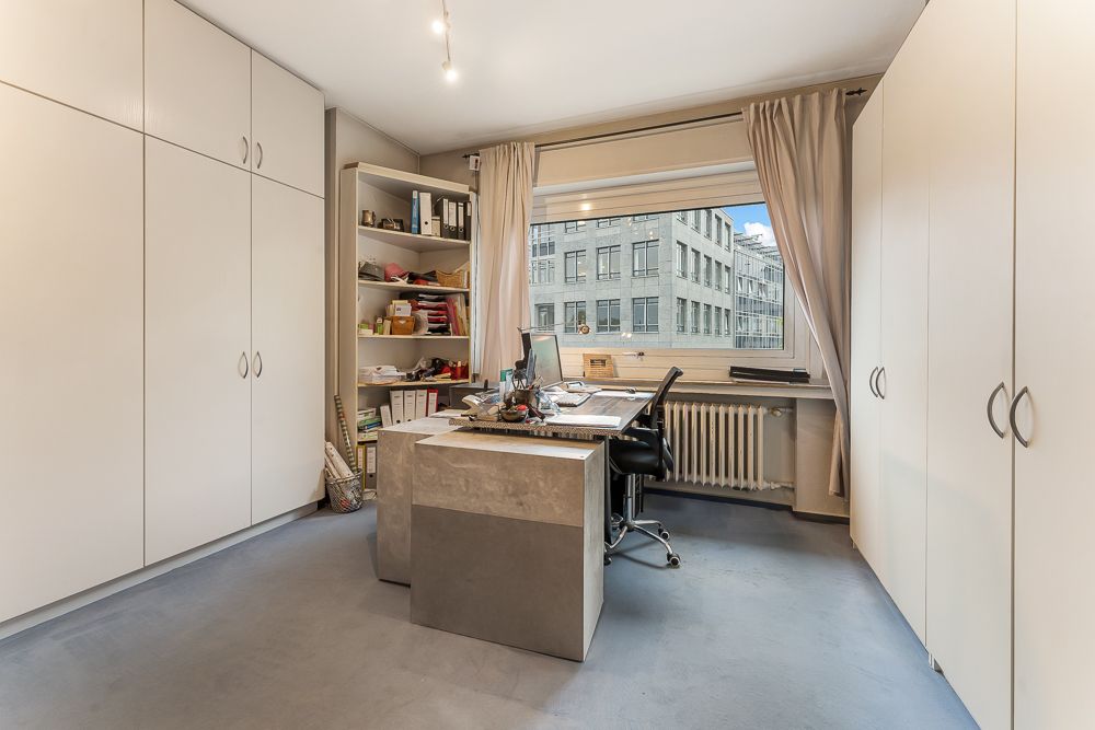 Helles Arbeitszimmer mit großem Schreibtisch, Regalen, Schränken und Fenster mit Blick nach draußen.