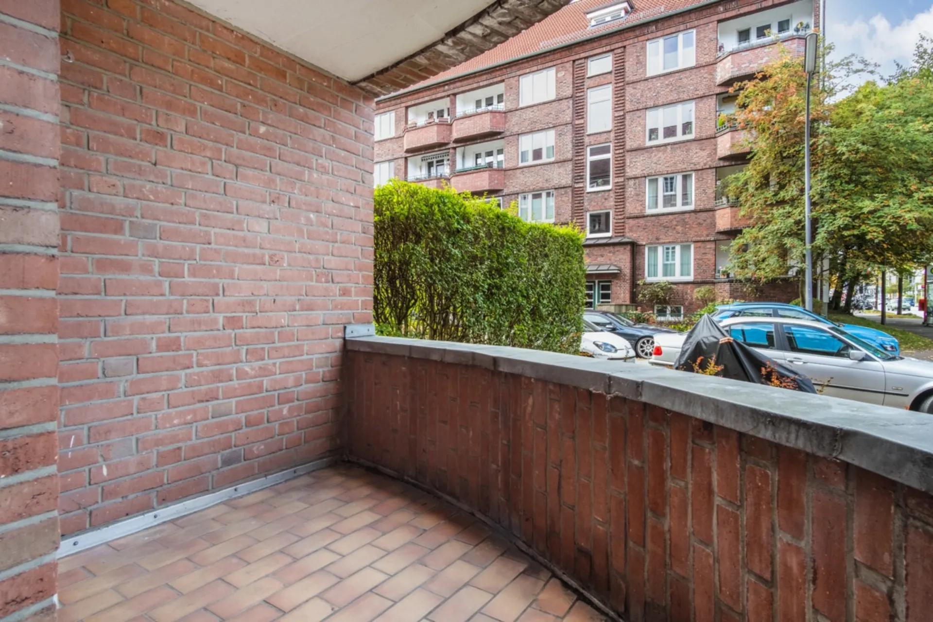 Überdachter Balkon mit Backsteinmauern und Blick auf parkende Autos und Wohngebäude.