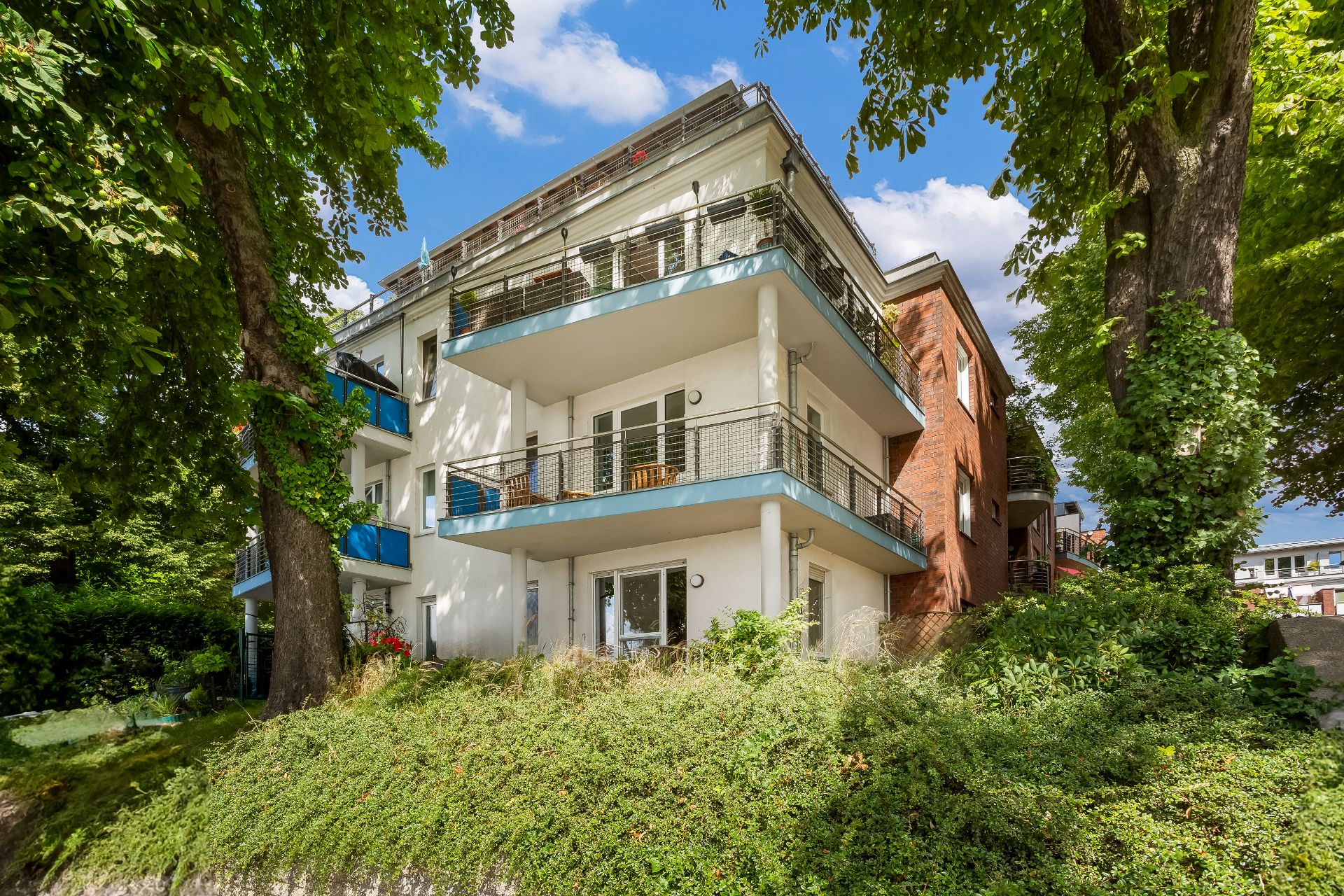 Mehrstöckiges Wohnhaus mit Balkonen, umgeben von Bäumen und Grünflächen.