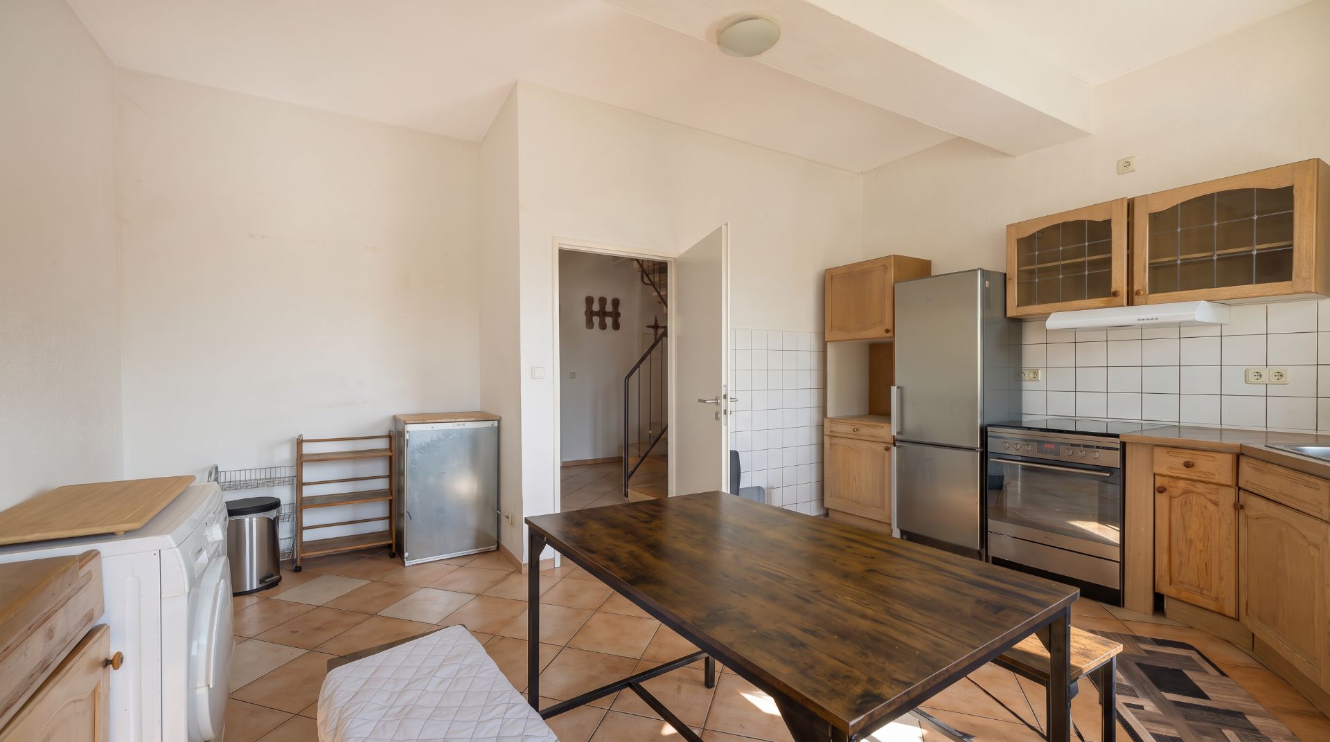Helle Küche mit Holzmöbeln, Esstisch, Kühlschrank, Herd und Waschmaschine.