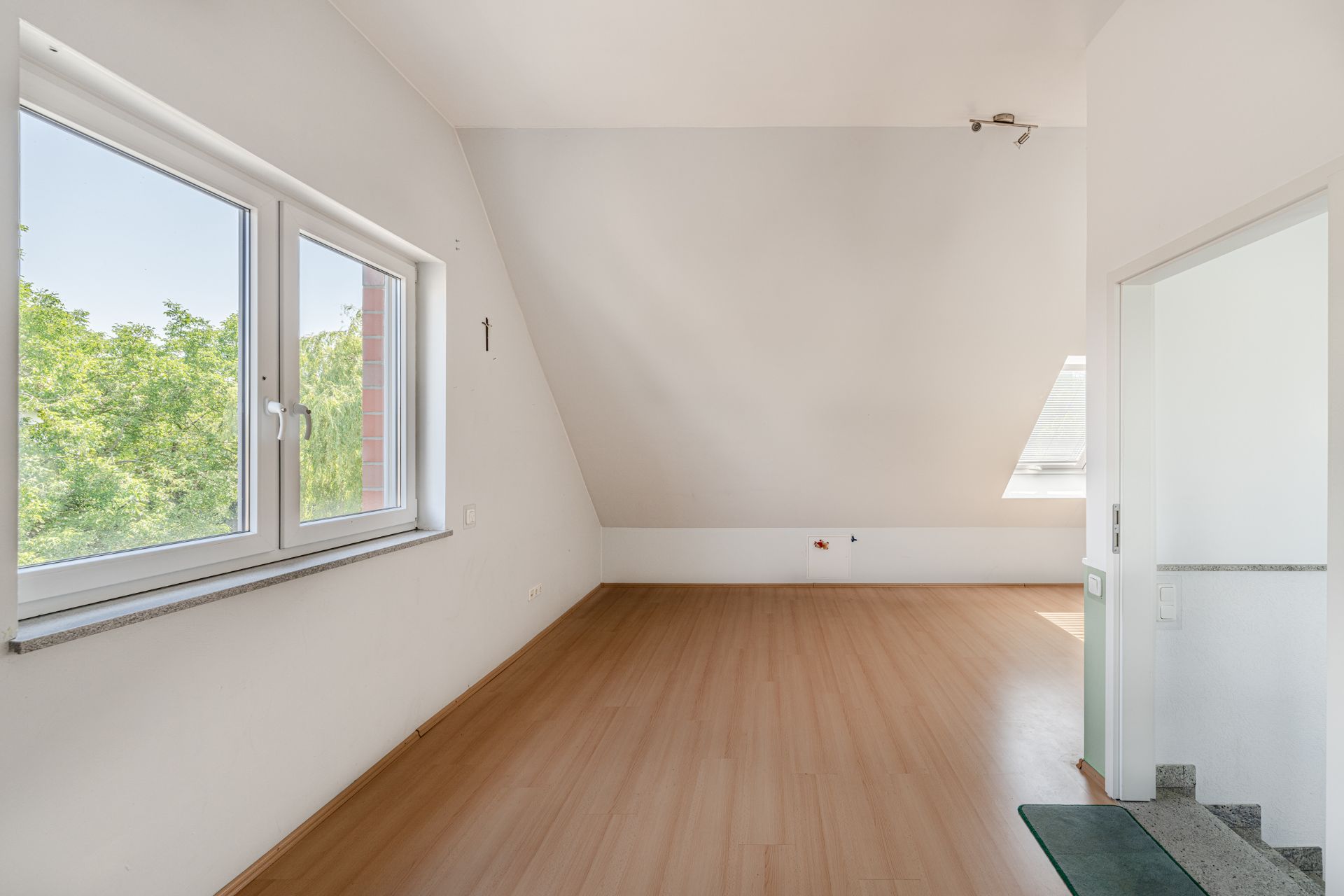 Heller, leerer Raum mit Dachschräge, großem Fenster und Laminatboden.