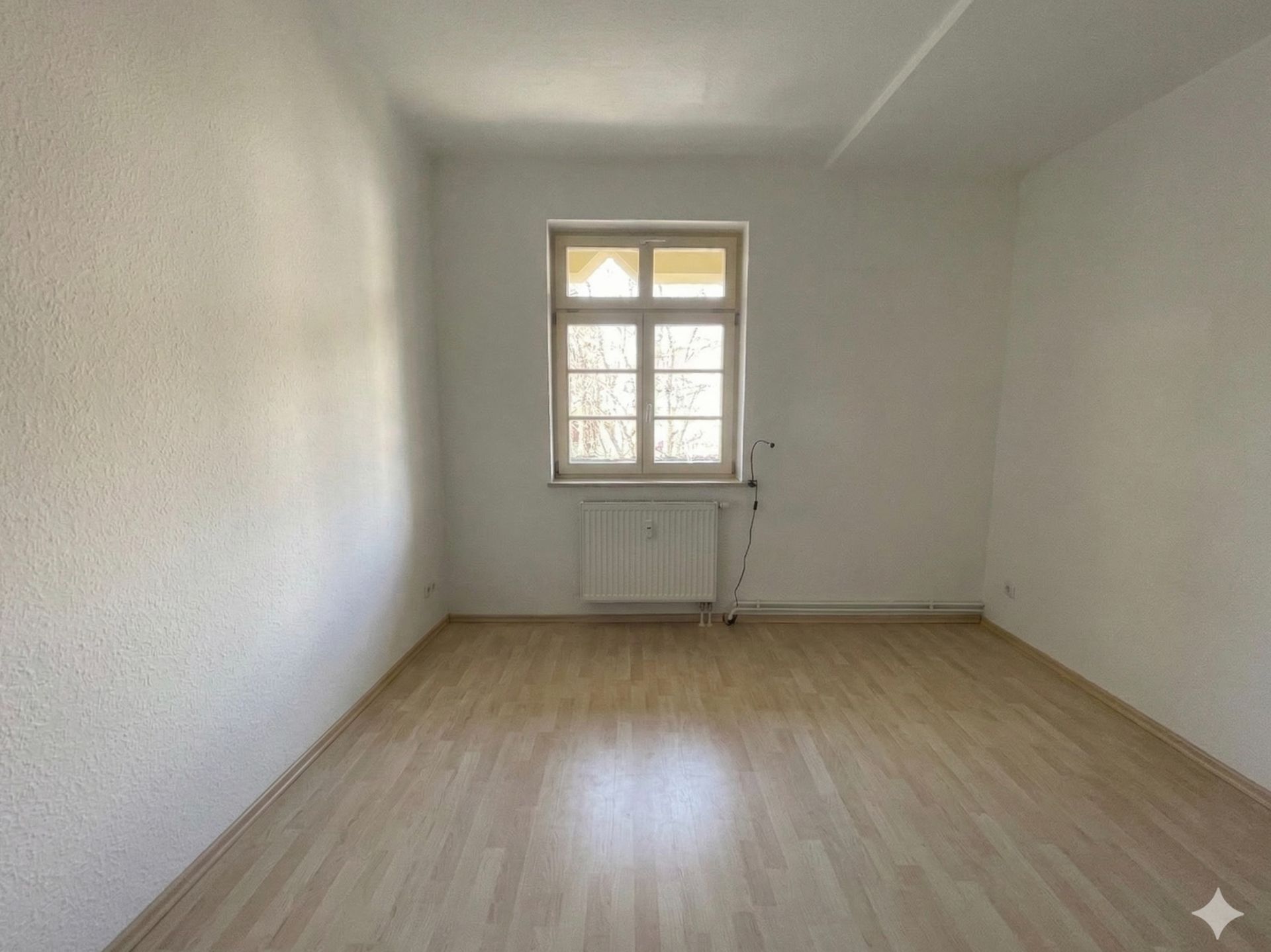 Leerer Raum mit hellem Holzfußboden, weiß gestrichenen Wänden und Fenster.