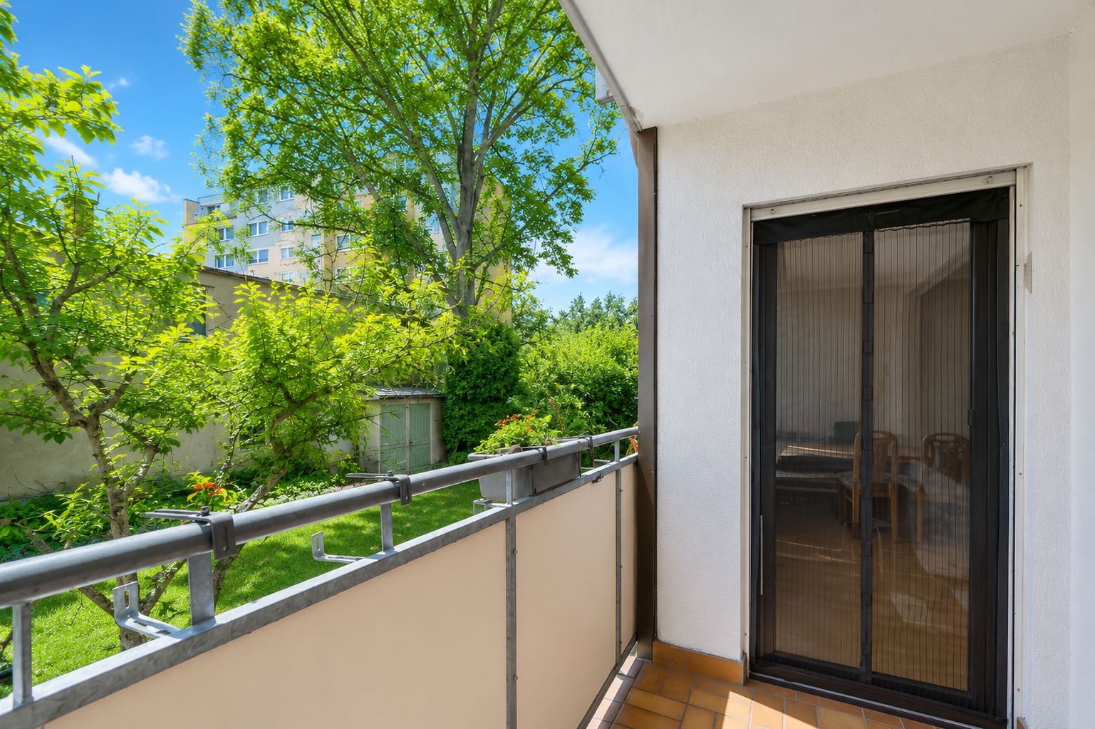 Balkon mit Glas-Schiebetür, Blick auf Garten mit Bäumen und Rasen.
