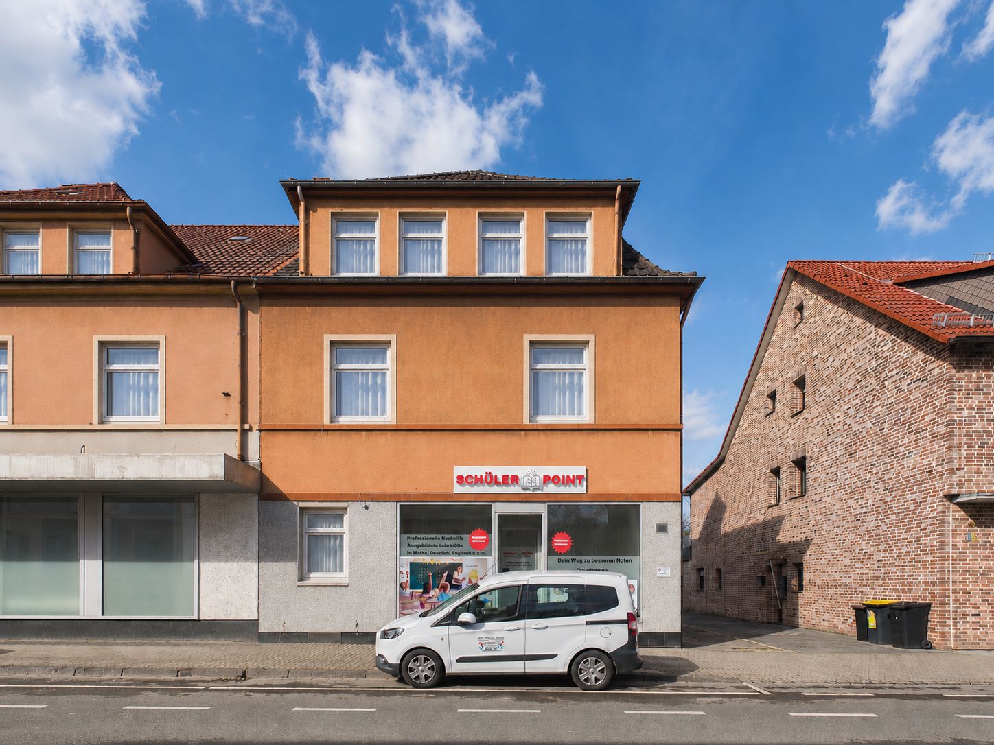 Orange Wohnhaus mit Schaufenster im Erdgeschoss und geparktem weißen Auto davor.
