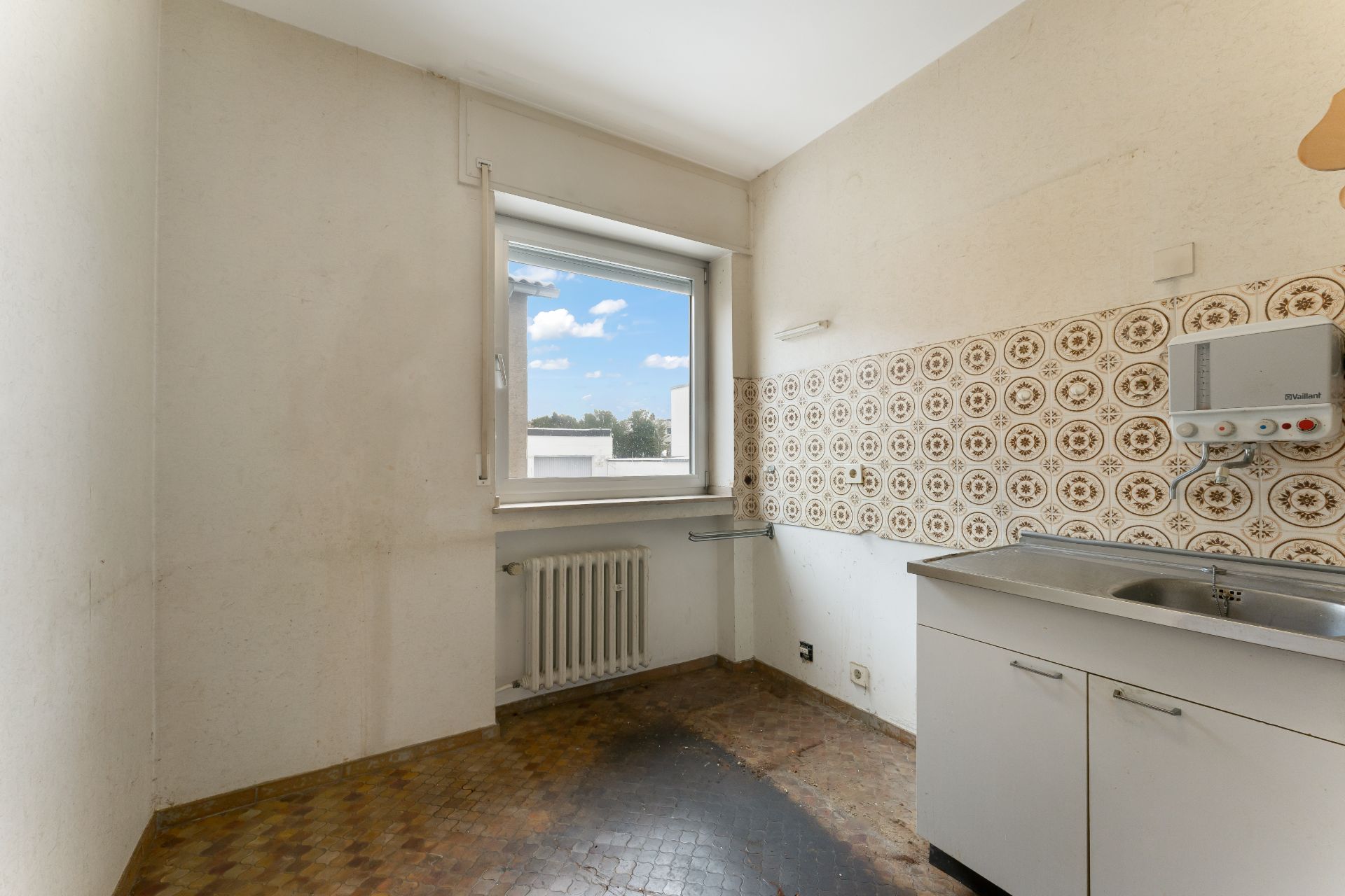 Leere Küche mit Fenster, Spüle und gemusterter Fliesenwand.