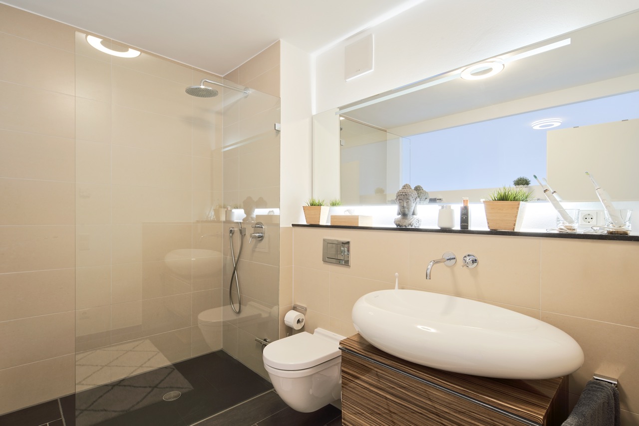 Modernes Badezimmer mit großer Dusche, Wandtoilette und Waschbecken vor großem Spiegel.