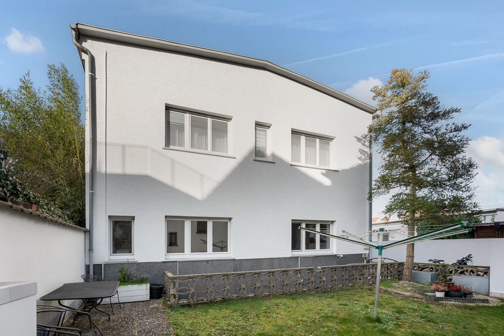 Hinteransicht eines weißen Wohnhauses mit Garten, Terrasse und Wäschespinne.