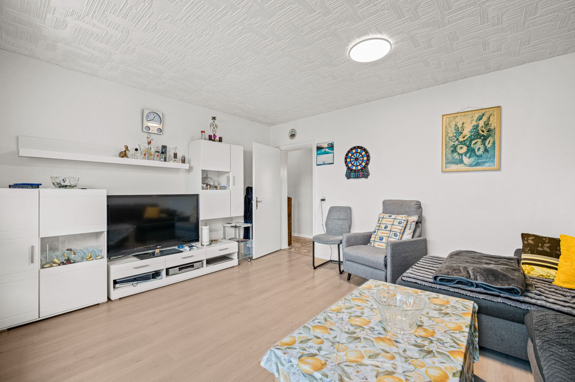 Wohnzimmer mit grauem Sofa, Fernseher, weißen Möbeln und Wanddeko, hell und ordentlich eingerichtet.