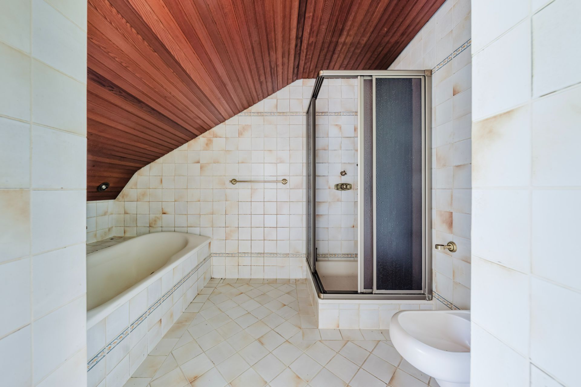 Bad mit Badewanne, Dusche und WC, weiße Fliesen und Holzdecke.