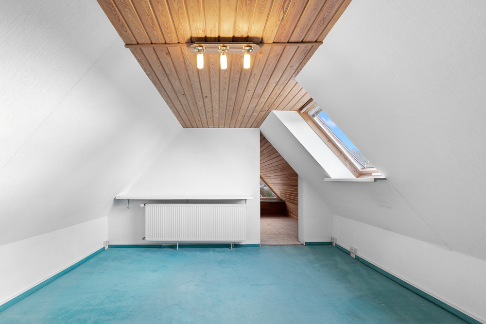 Dachzimmer mit schrägen Wänden, blauem Boden, Holzdecke und Dachfenster.