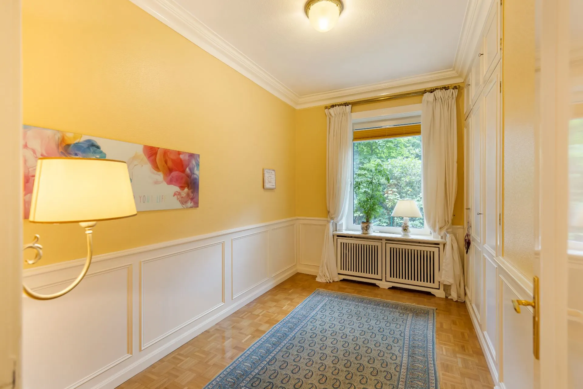 Heller Flur mit gelben Wänden, Teppich, Fenster mit Vorhängen und Tischlampe.