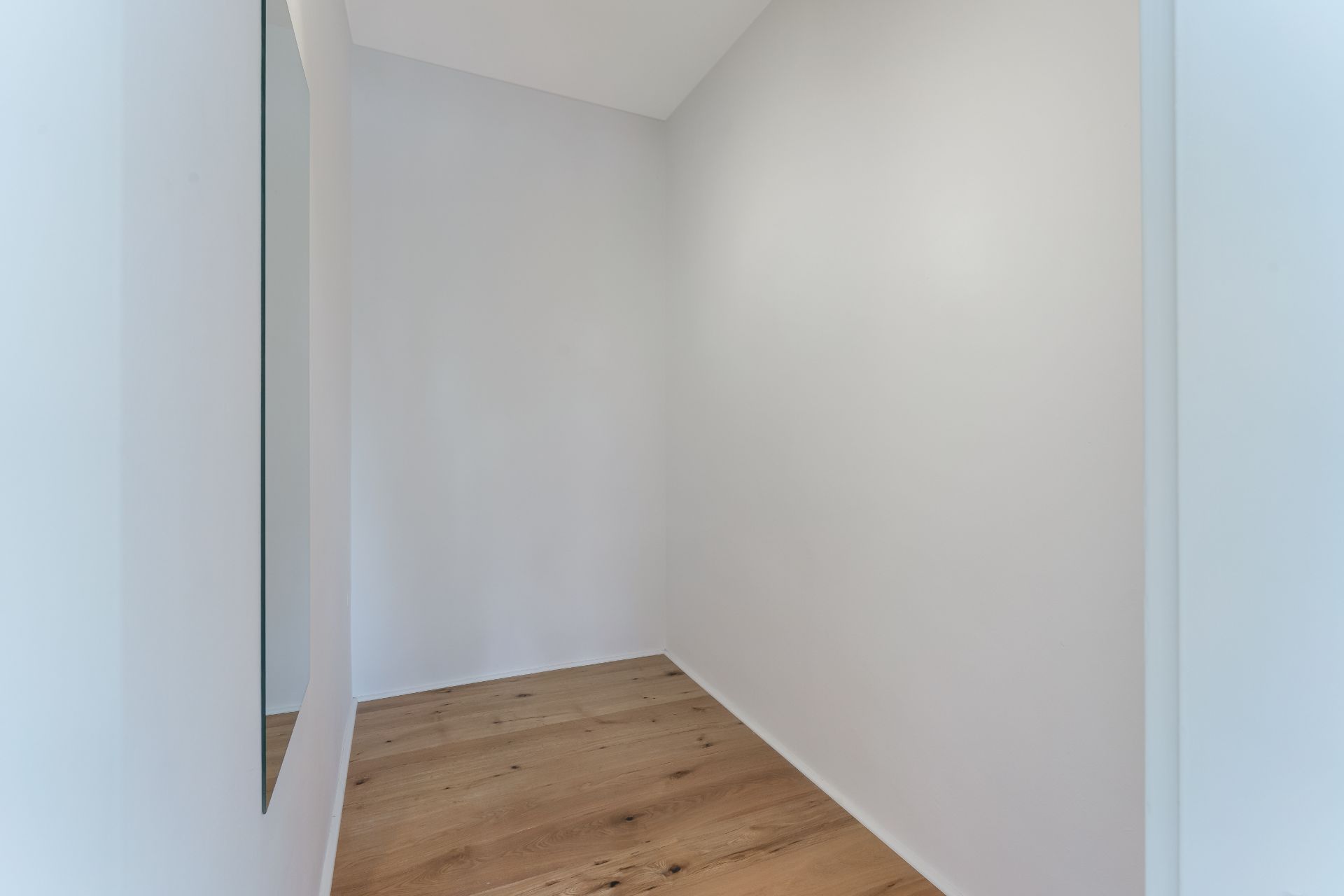 Kleiner, leerer Flur mit weiß gestrichenen Wänden und Holzfußboden, Spiegel an der Wand.