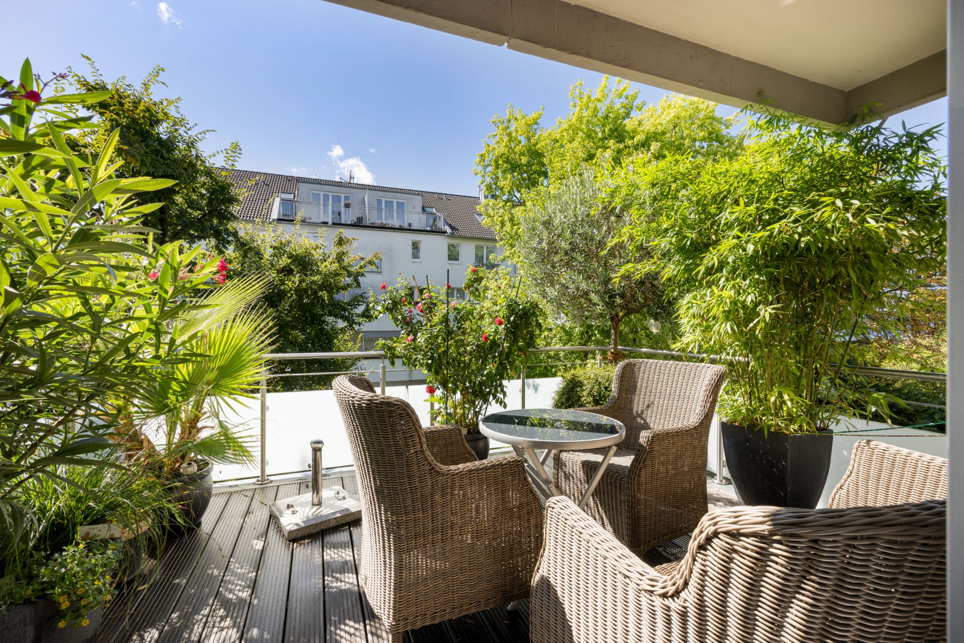 Überdachter Balkon mit vier Korbstühlen, kleinem Glastisch und vielen grünen Pflanzen.