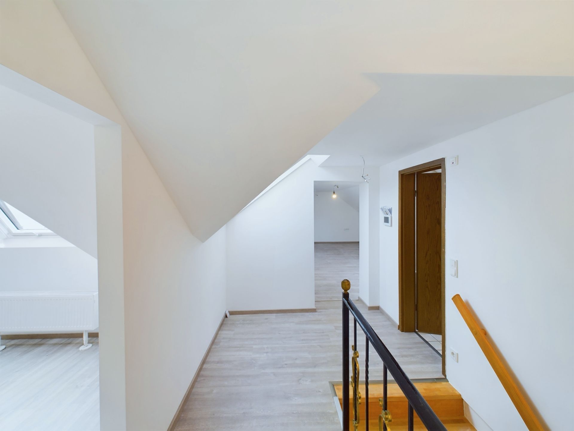 Heller Flur mit Dachschräge, Holztreppe und offenem Zugang zu weiteren Räumen.