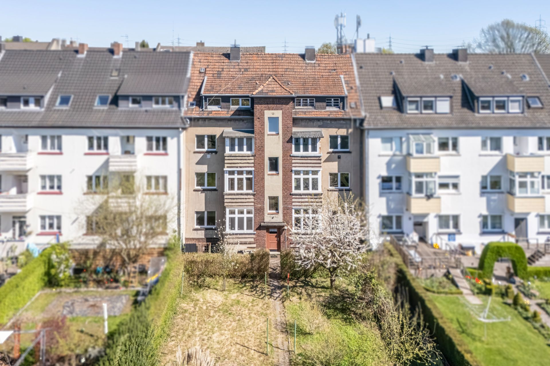 Mehrfamilienhaus mit Vorgarten und Bäumen, umgeben von ähnlichen Wohnhäusern.