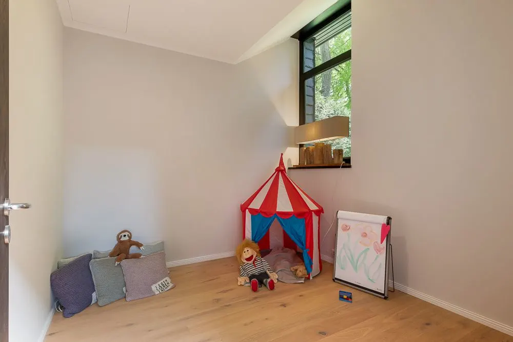 Kinderzimmer mit Zirkuszelt, Kissen, Kuscheltier, Puppe und Staffelei mit Kinderzeichnung.